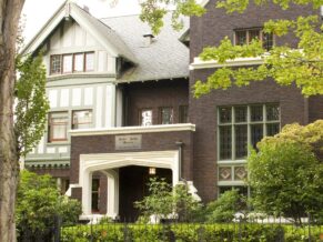 The outside of the Shafer Baillie Mansion shows lush gardens and a rod iron fence boardering this Tudor-revival home with period accents.