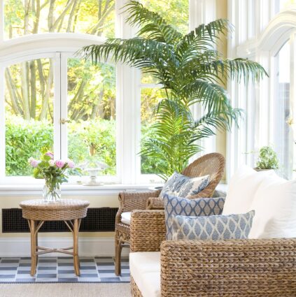 Large leafy palms and light couches rest in the bright and sunny atrium with large glass windows that look out over the gardens.