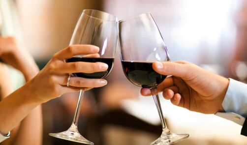 Two hands holding wine glasses filled with red wine cheer.